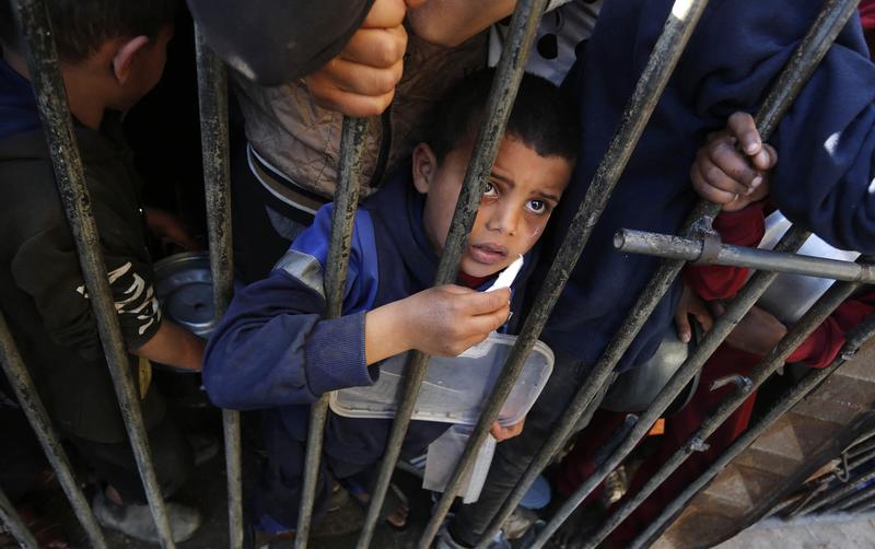 Copii palestinieni stau la coadă pentru a primi alimente, distribuite de organizațiile umanitare, în timp ce atacurile israeliene continuă în Deir al-Balah, Fâșia Gaza, pe 12 martie 2024.