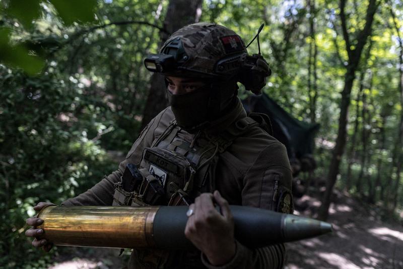 Un soldat ucrainean transportă un obuz de artilerie pe front