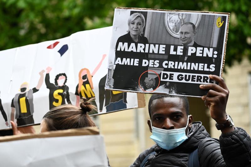 un protestatar arata o pancarta care o arata pe Marine Le Pen dand mana cu Vladimir Putin